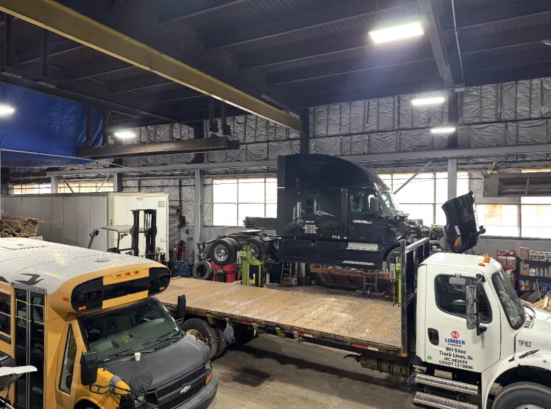 The Top Guns shop floor with a school bus, a fleet flatbed, and a semi with the hood open.