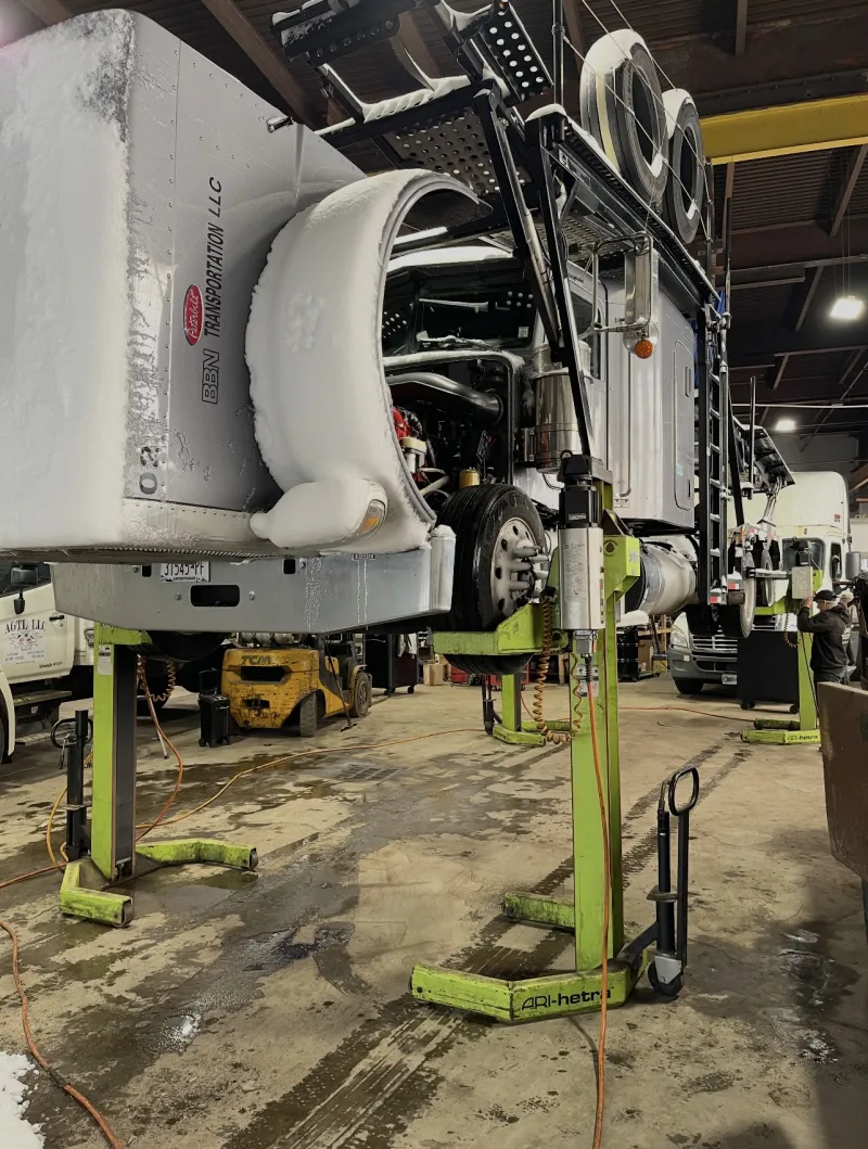 Peterbilt raised on column lifts so the suspension and undercarriage can be reached.