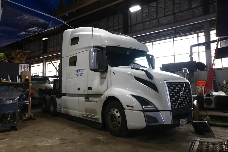 White Volvo tractor in the shop with the front bumper removed for repair.
