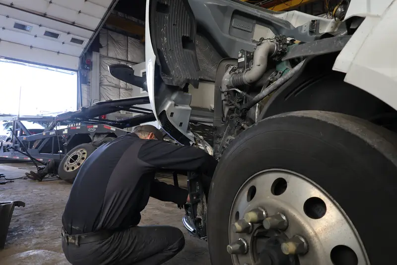 Mechanic working in the open engine bay of a white Volvo tractor.