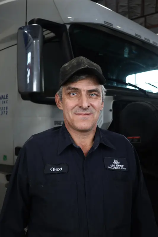 Olexi, a Top Guns mechanic, standing in front of a white semi in the shop.