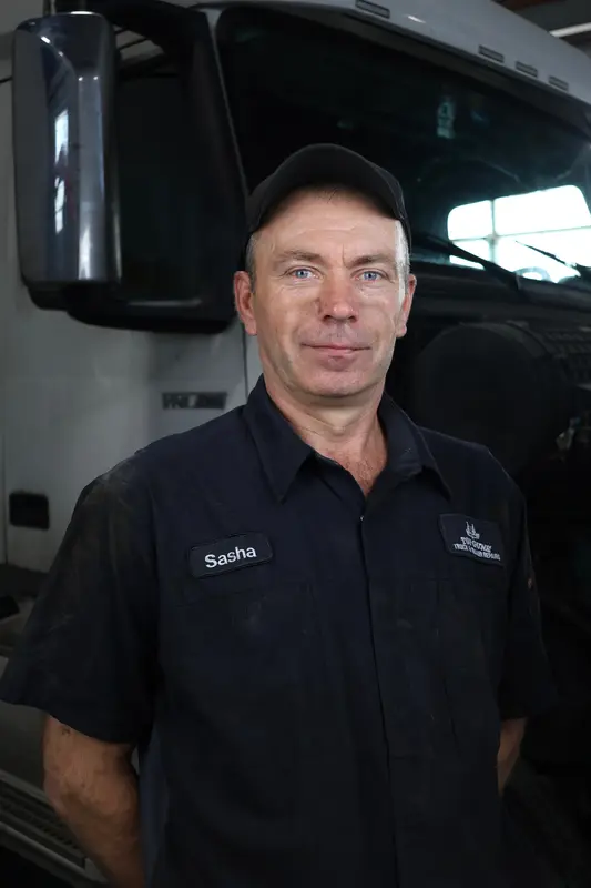 Alex, a Top Guns mechanic, standing in front of a white Volvo in the shop.