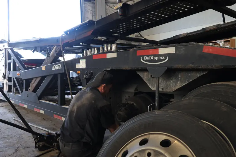 Mechanic working the wheel and axle of a car-hauler trailer.