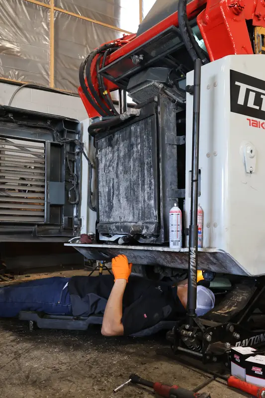 Mechanic under a Takeuchi TL loader with the radiator exposed.