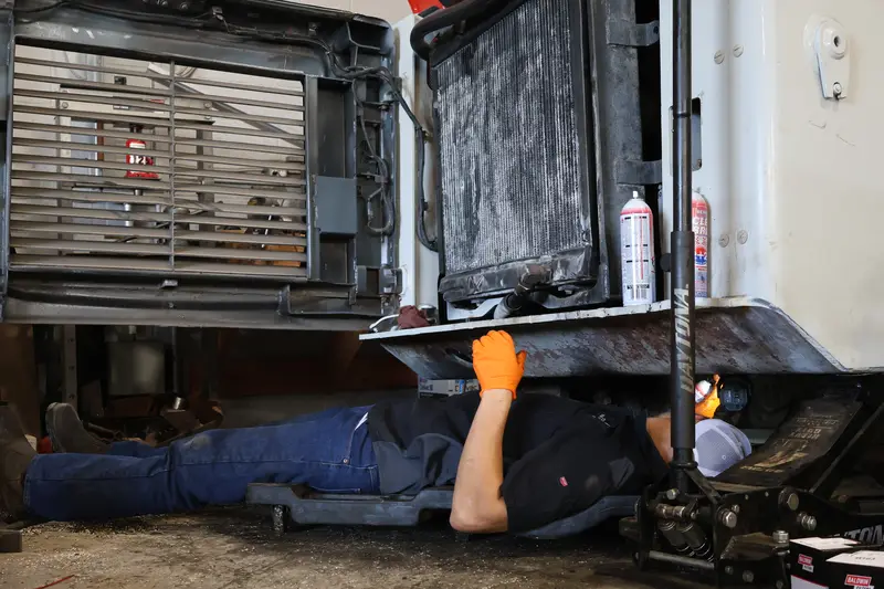 Mechanic on a creeper under a Takeuchi track loader with the rear open.