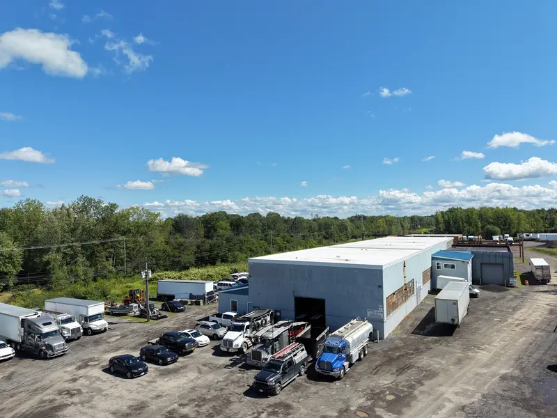 Wider aerial of the shop building, yard, and commercial vehicles.
