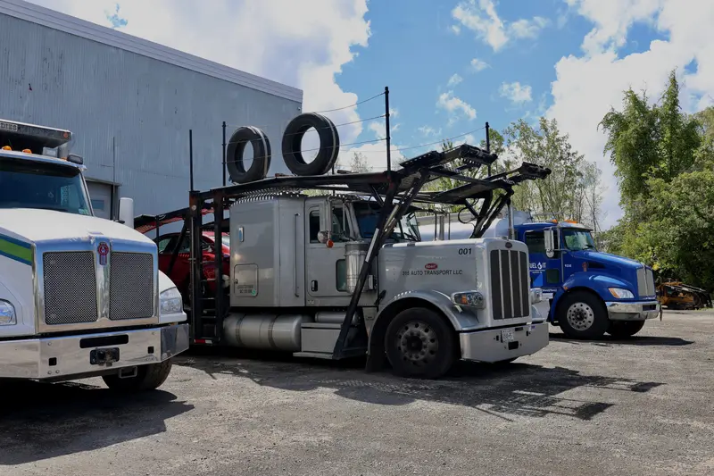 Silver Peterbilt car hauler parked between two Kenworths in the shop lot.