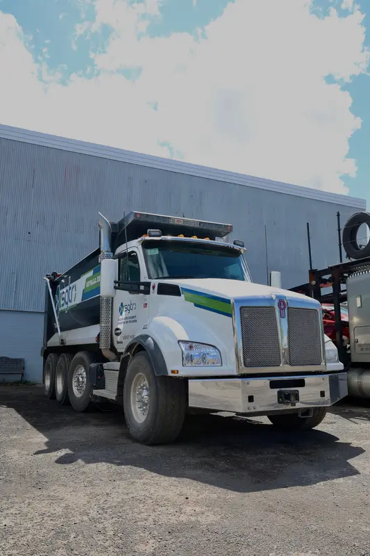 Low-angle shot of the white Kenworth dump truck against the shop wall.
