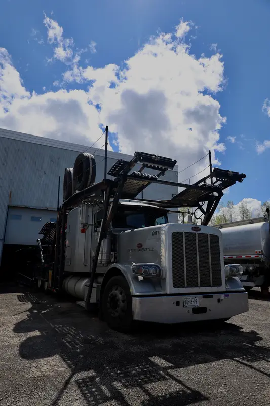Silver Peterbilt car hauler in the lot with the shop building behind it.