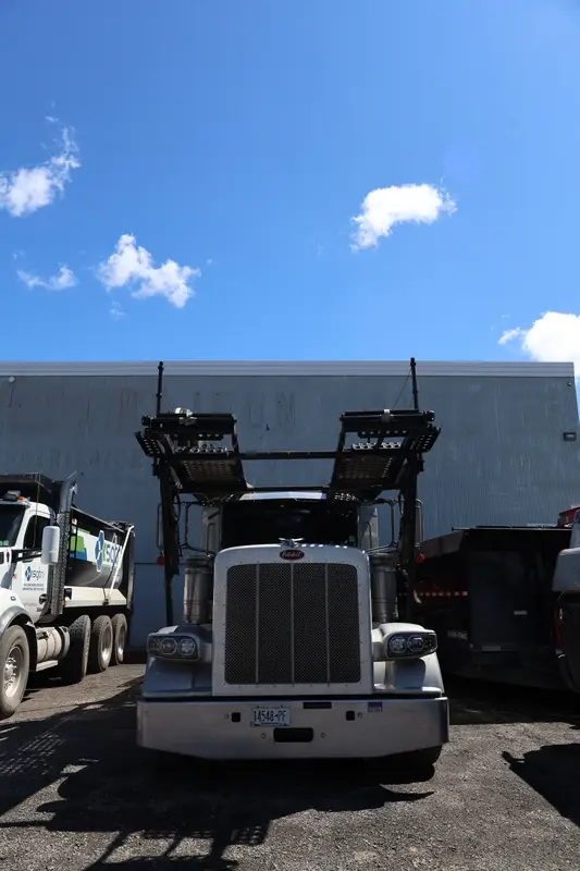 Head-on view of the silver Peterbilt car hauler in the shop lot.